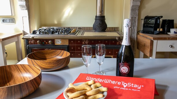 A kitchen with a wooden bowl, a plate of breadsticks, a bottle of wine, and two glasses. - Wondrous Palazzetto 1619 in Magical Burano Island (Burano)