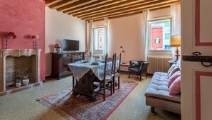 A cozy living room with a fireplace, a dining table with chairs, a sofa, and a television. - Wondrous Palazzetto 1619 in Magical Burano Island (Burano)