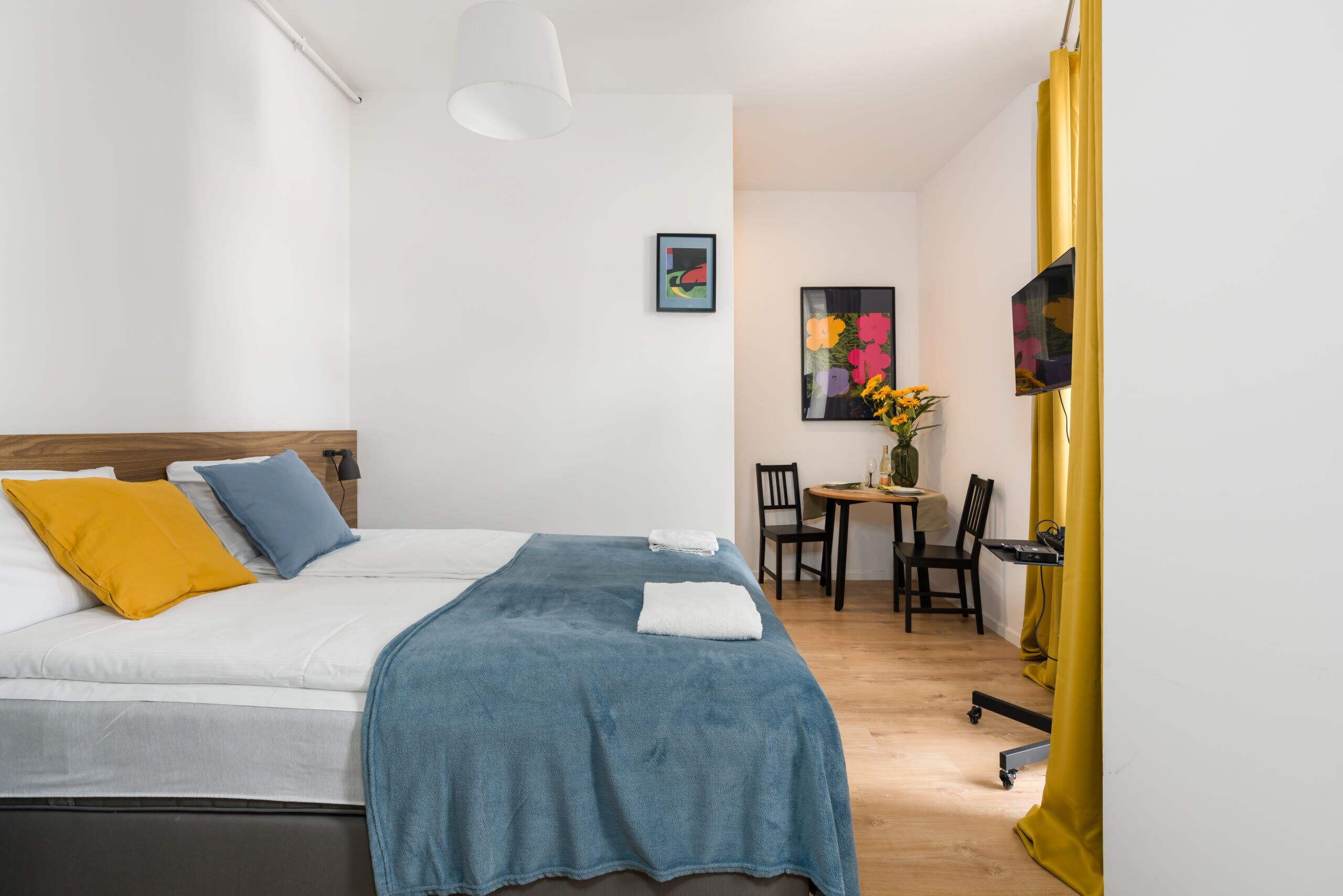 A cozy bedroom featuring a double bed with blue bedding and yellow accents, complemented by modern decor.
