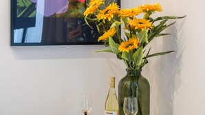 Een eettafel met een vaas geel bloemen, een fles wijn en een glas.