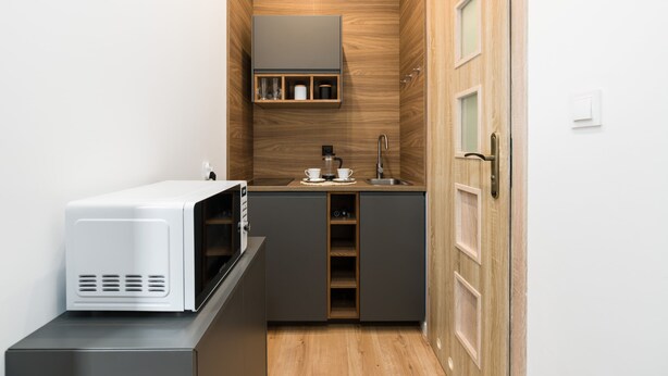 Een compacte keuken met een magnetron op een aanrecht, een spoelbak en een houten kast met planken.