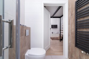 Un baño moderno con inodoro blanco, tocador de madera y zona de ducha.