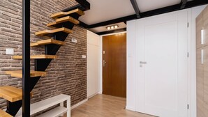 Un intérieur moderne avec un escalier en bois adossé à un mur de briques, un banc blanc et une porte en bois.