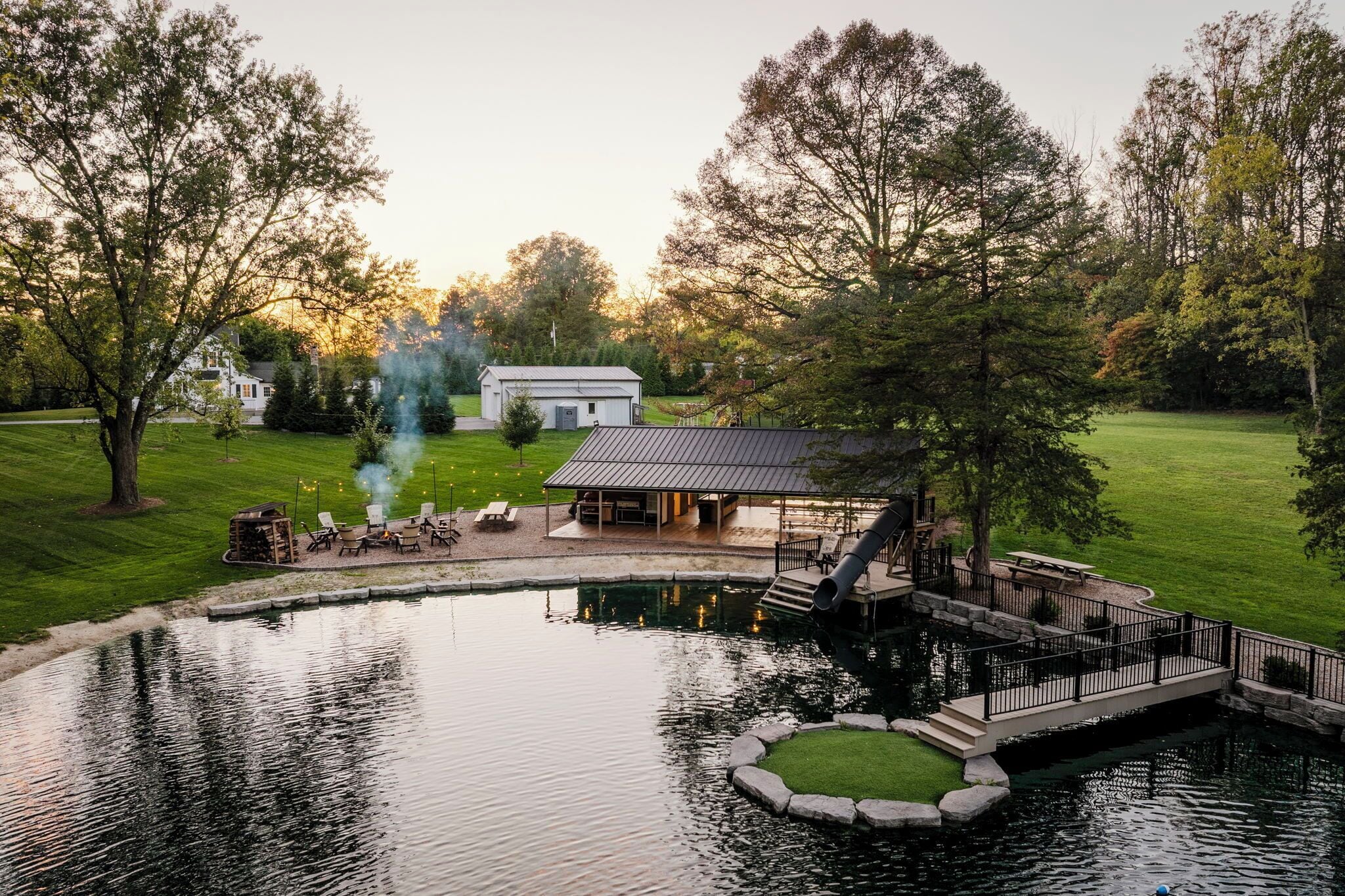 A pond with a gazebo, a small building, and a white house in the background.