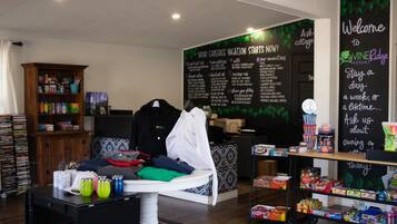 A room with a bed, a table with drinks, a shelf with snacks, and a chalkboard with information.