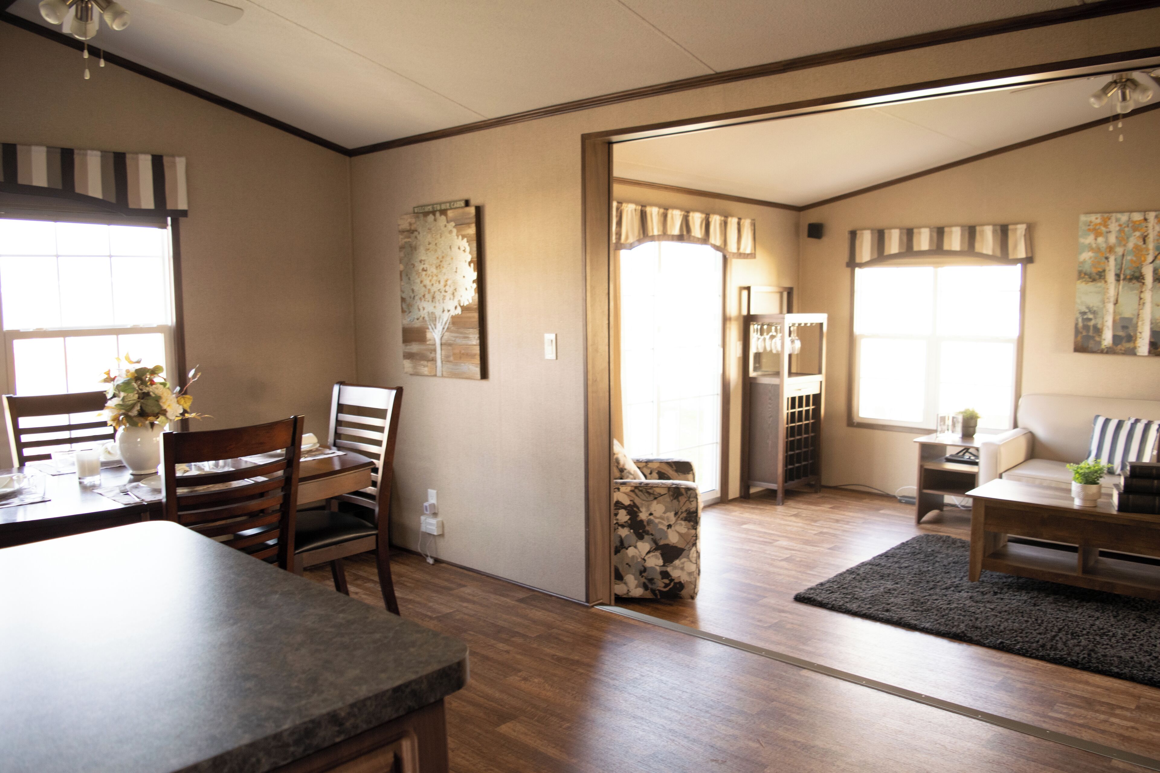 A spacious living area with a dining table, chairs, a sofa, and a coffee table. There is a large window providing natural light, and a door leading to another room.
