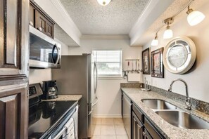 A compact kitchen with a microwave, stove, and sink. There is a window providing natural light and a view of the outside.