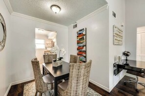 A dining area with a dark wooden table, wicker chairs, and a modern abstract painting. - I22 - Apt|Yard|11mi to Fair Park|Sleeps 4 (Irving)