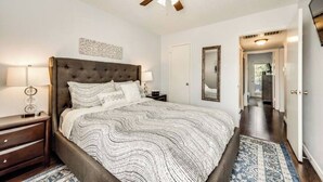 A bedroom with a large bed, a ceiling fan, a nightstand, and a bedside table.