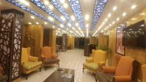 A hotel lobby with yellow armchairs, a coffee table, and a TV mounted on the wall. - Rendezvous hotel petra (Wadi Musa)