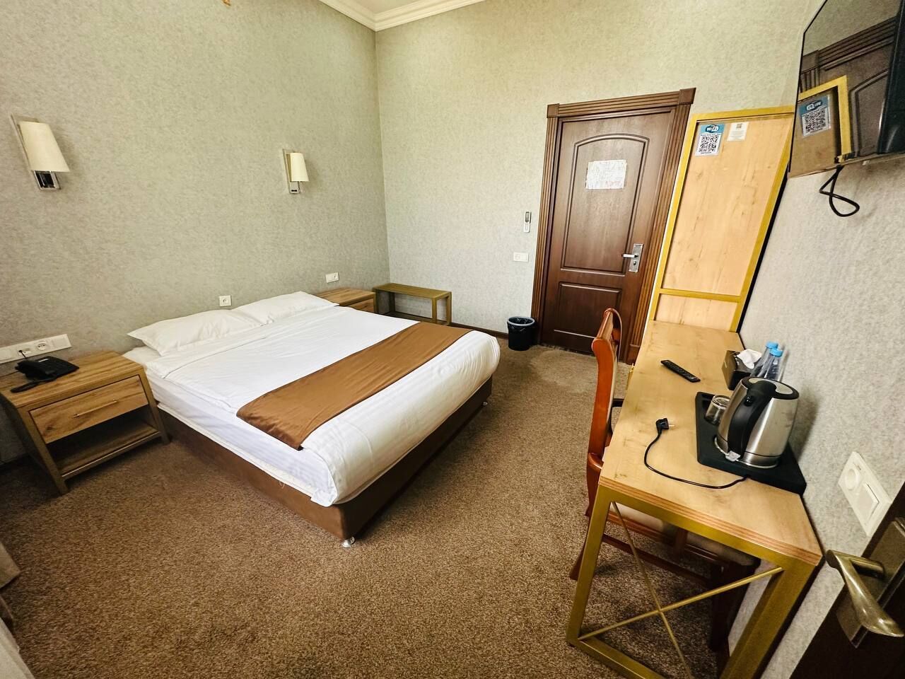 A hotel room with a bed, bedside table, desk, chair, and a mirror.