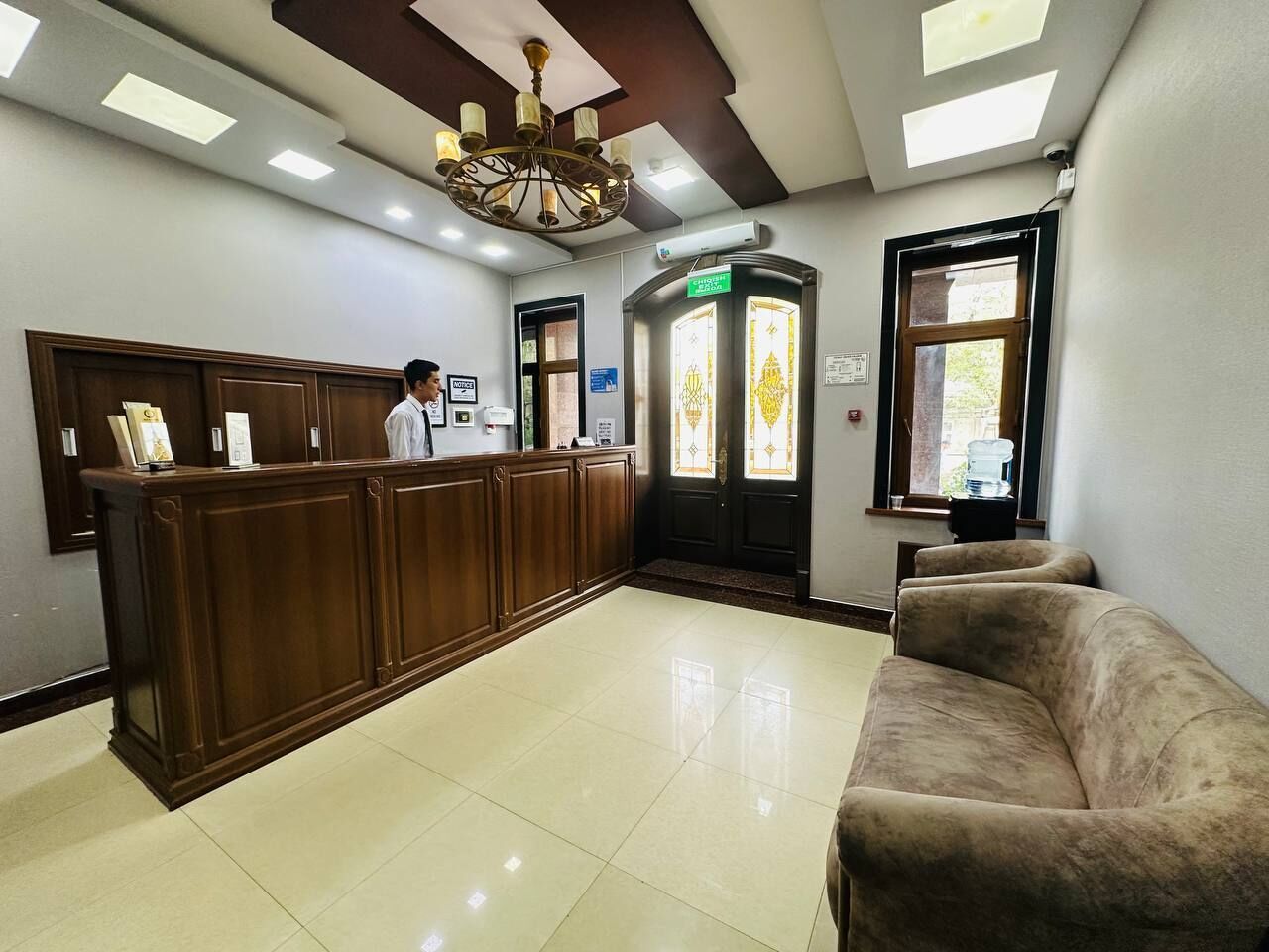 A reception area with a wooden counter, a receptionist, a couch, and a chandelier.