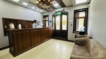 A reception area with a wooden counter, a receptionist, a couch, and a chandelier.