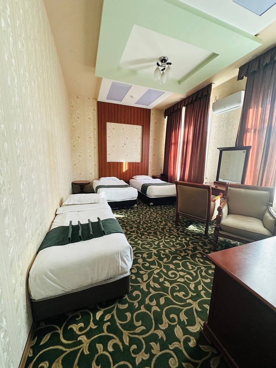 A hotel room with three single beds, a desk, a chair, a television, and a ceiling fan.