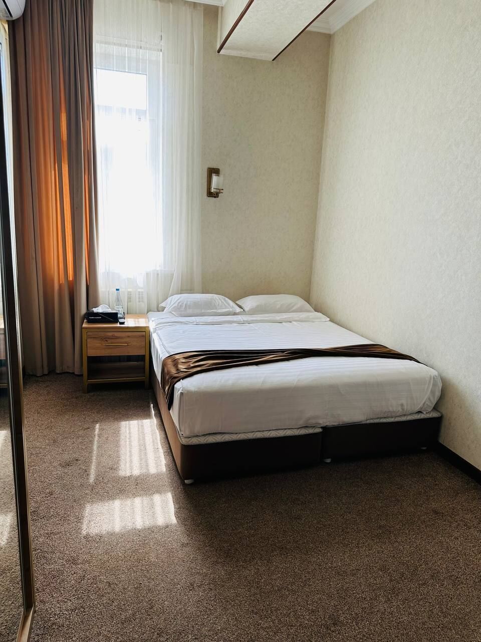 Ein Hotelzimmer mit einem Bett, einem Nachttisch, einer Lampe und einem Fenster mit Vorhängen.