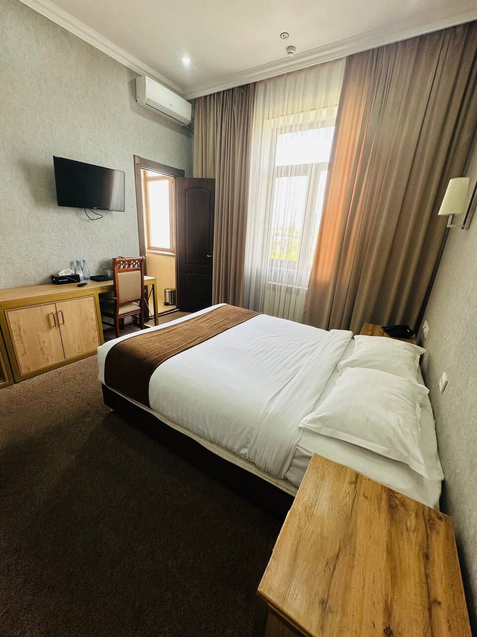 A hotel room with a bed, a desk, a chair, a television, and a window with curtains.