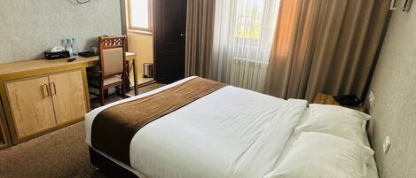 A hotel room with a bed, a desk, a chair, a television, and a window with curtains.