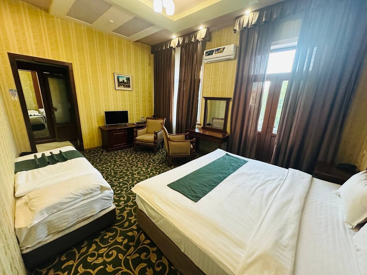 A hotel room with two beds, a desk, a chair, a TV, and a mirror.