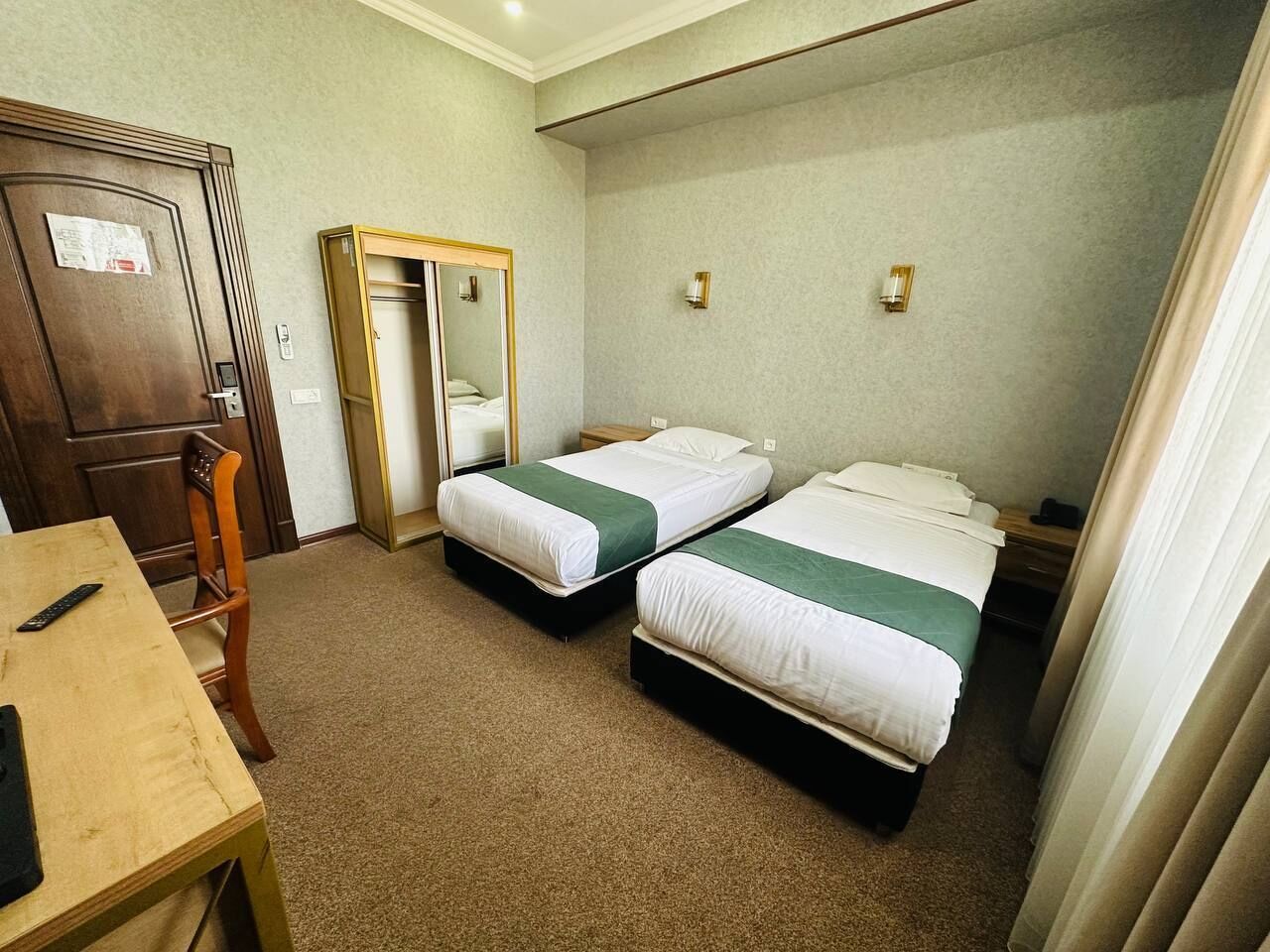 Une chambre d’hôtel avec deux lits, un bureau en bois, un miroir et une porte.