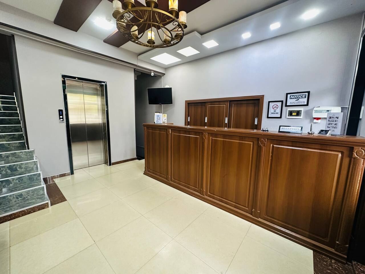 Una zona de recepción con mostrador de madera, una escalera, un ascensor y un televisor instalado en la pared.