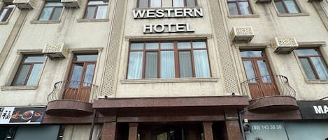 Ein Hotel im Westernstil mit einem zentralen Eingang, mehreren Fenstern und einem mit Fliesen belegten Bürgersteig.