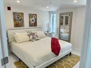 A bedroom with a bed, a nightstand, a mirror, and artwork on the walls.