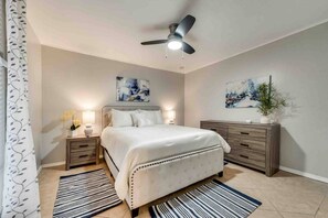 Une chambre à coucher comprenant un lit, des tables de chevet, une commode, un ventilateur de plafond et des œuvres d’art accrochées aux murs.