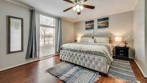 A bedroom with a bed, a ceiling fan, a window with curtains, and a nightstand with a lamp. - GP56 -  Stylish 3BD Condo | Six Flags| Grand Prairie (Grand Prairie)