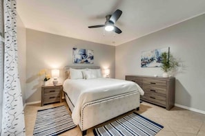 Une chambre à coucher comprenant un lit, des tables de chevet, une commode, un ventilateur de plafond et des œuvres d’art accrochées aux murs.