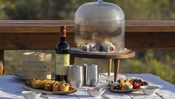 Una mesa dispuesta con comida y bebidas, incluyendo una botella de vino, un recipiente de madera y una cúpula de vidrio que cubre sushi.