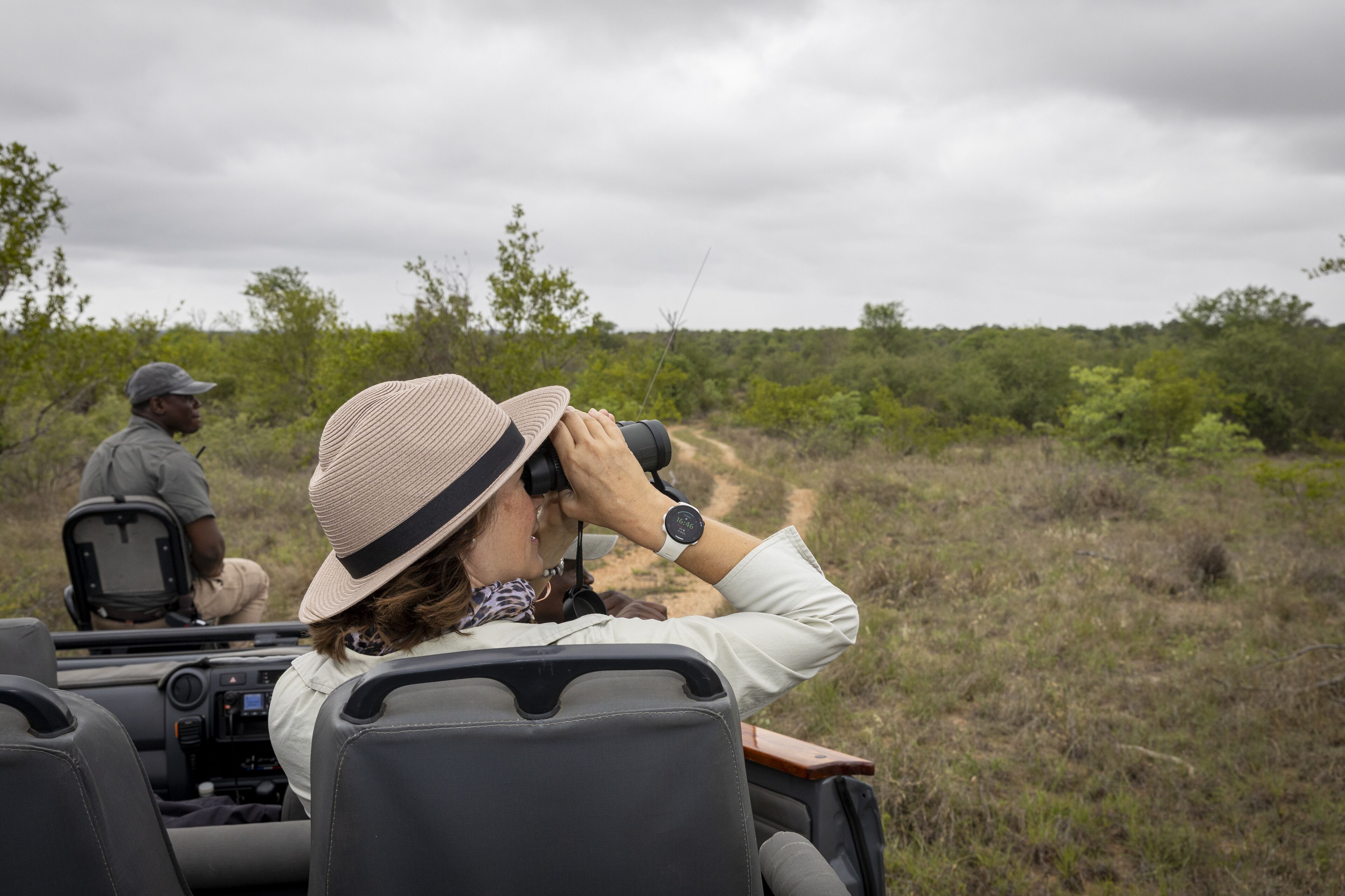 Het interieur van een safarivoertuig met twee passagiers, waarvan één een verrekijker gebruikt.
