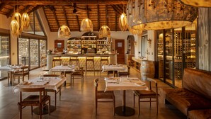 Un restaurante con mesas y sillas de madera, una zona de bar y una cava de vinos.