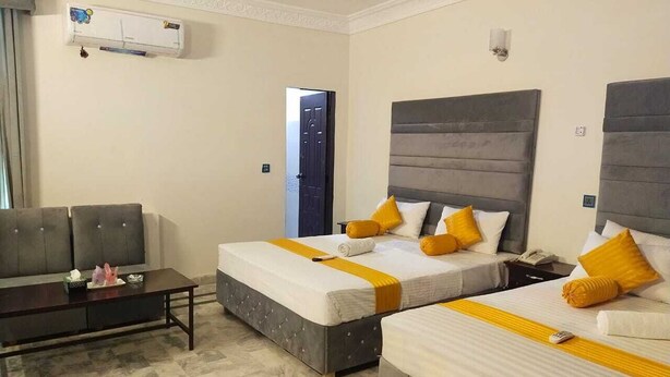A hotel room with two beds, a sofa, a small table, and an air conditioning unit. - Hotel Royal Grand (Mekhtar)