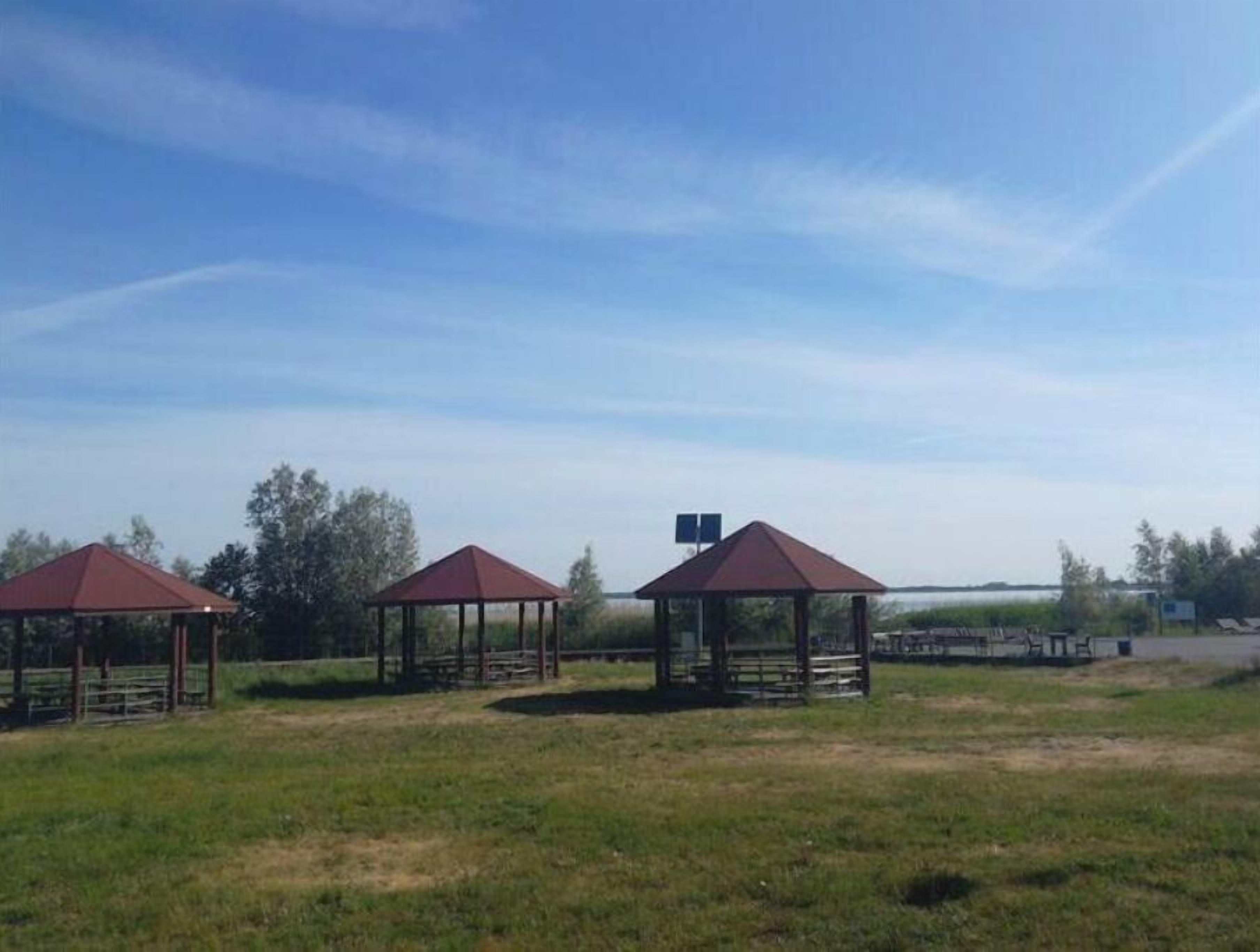 Three wooden gazebos with red roofs in a grassy field.