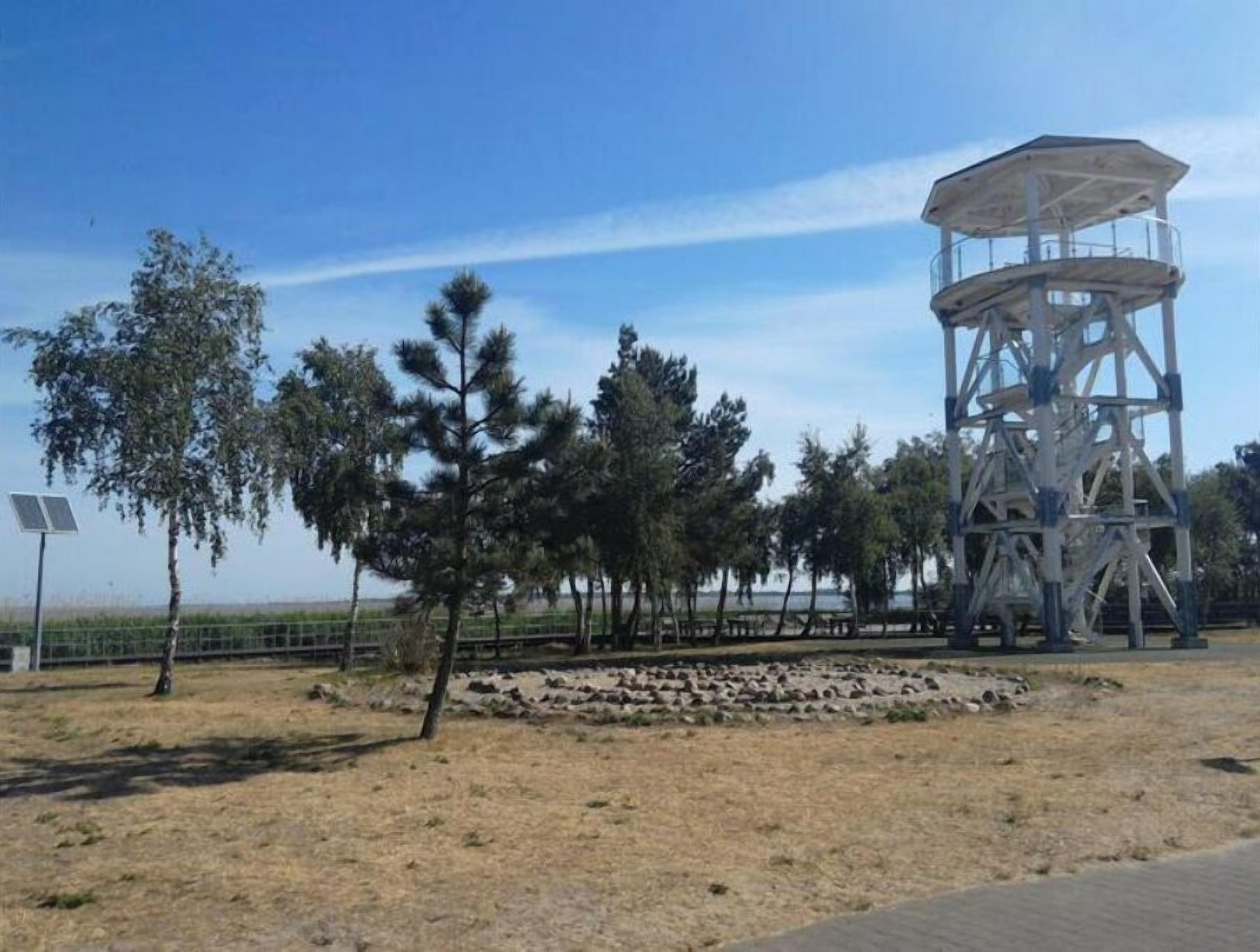 A metal observation tower with a viewing platform, surrounded by trees and a fenced area.