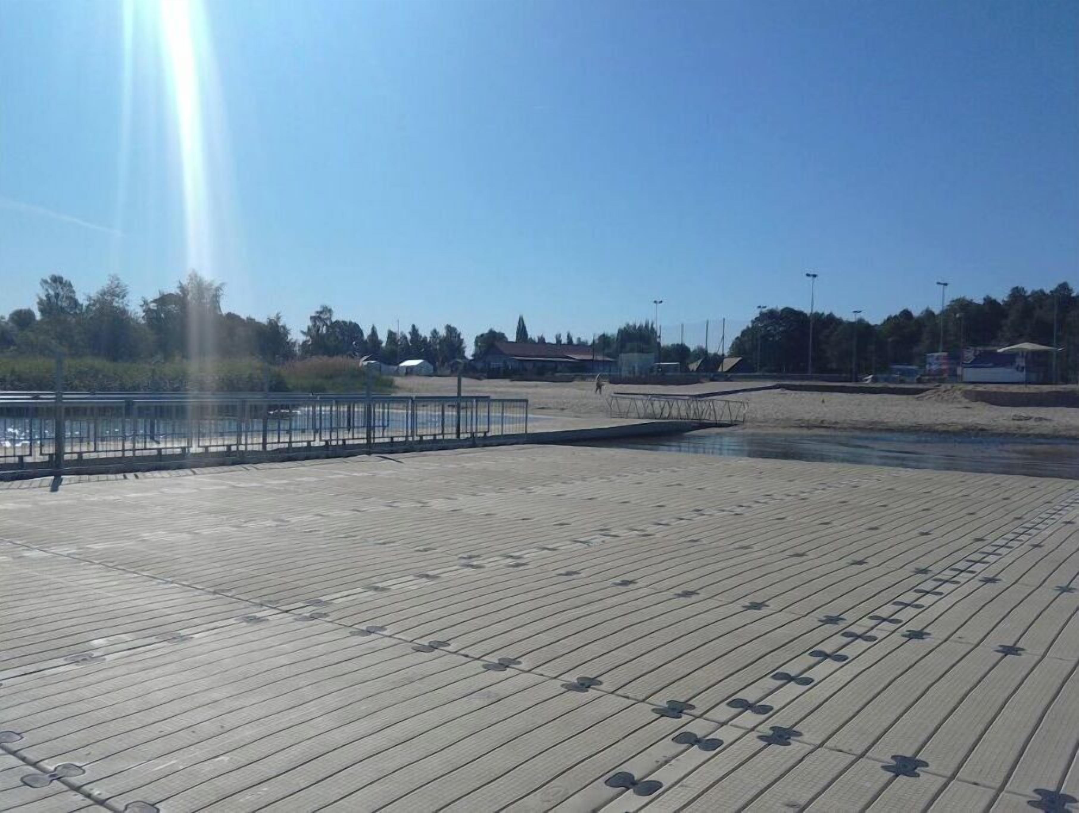 Un muelle de madera que conduce a una zona de playa, con barandilla metálica y un pequeño embarcadero.