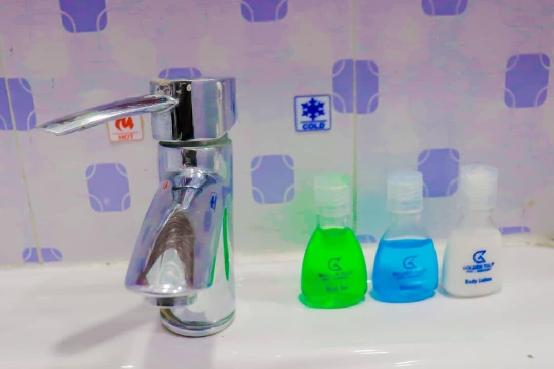 A bathroom sink with a chrome faucet, three bottles of liquid soap, and a "HOT" sign on the wall.