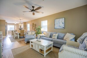 Un salon spacieux doté d’un ventilateur de plafond, un coin repas avec une table et des chaises, et une grande fenêtre avec des stores.