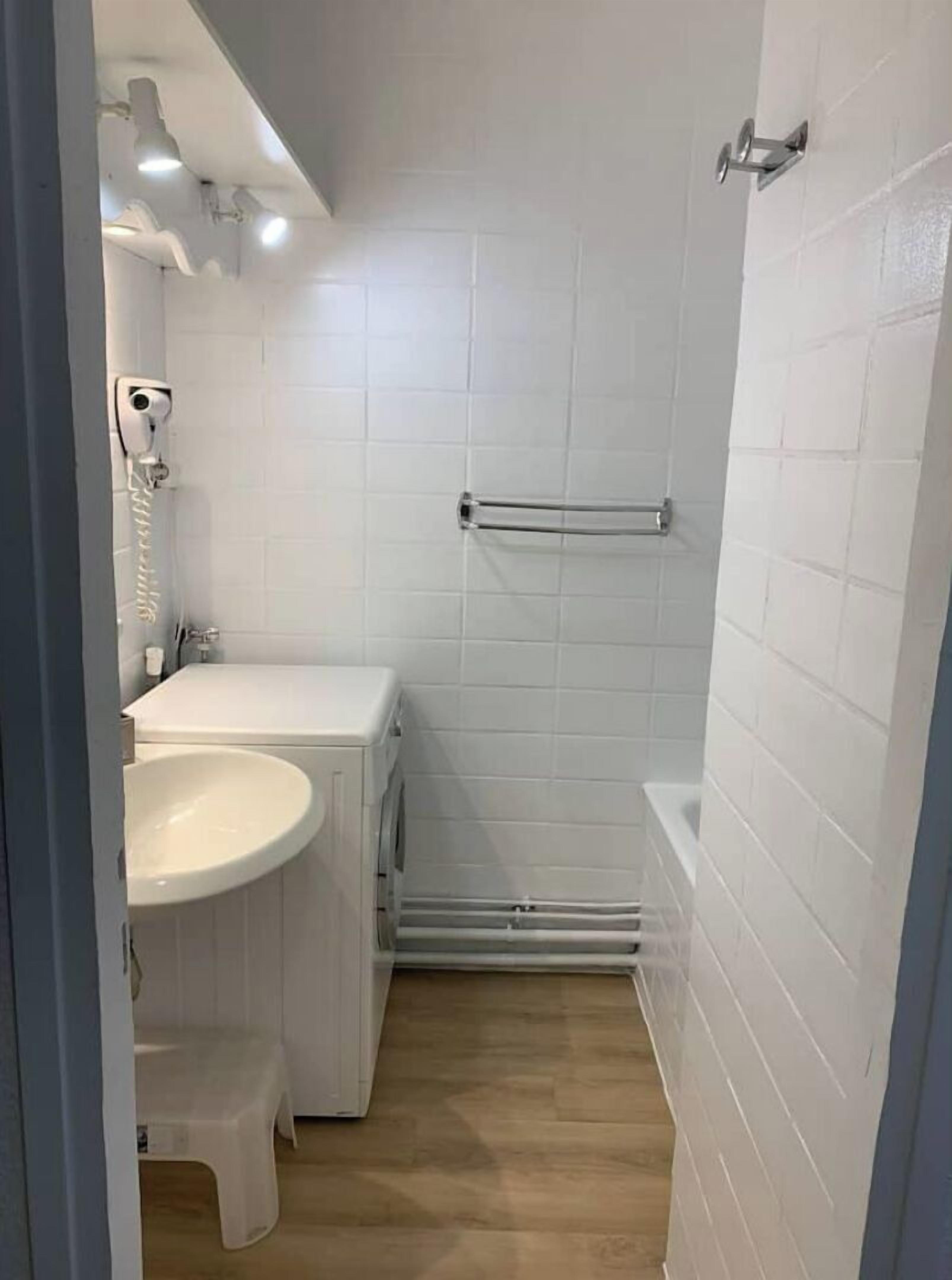 Un bany petit i modern amb rajoles blanques, un lavabo, un vàter i una zona de dutxa.