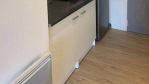 Ett litet pentry med mikrovågsugn, kylskåp och en hylla i trä.