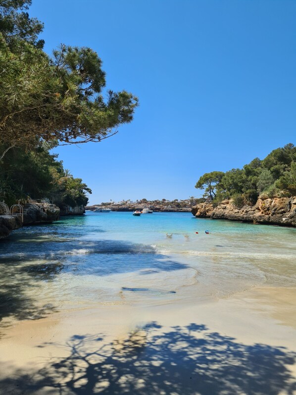 A coastal scene with clear turquoise water, sandy beach, and rocky cliffs.