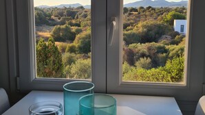 A room with a large window overlooking a landscape with trees and hills. There are three glass candle holders on the windowsill.