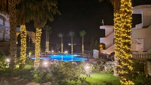 A pool area with multiple swimming pools, surrounded by palm trees and illuminated by string lights.