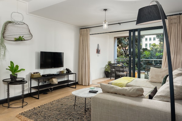 A modern living room with a flat-screen TV, a sofa, a coffee table, and a hanging plant.