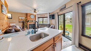 A kitchen with a large island, a ceiling fan, and a view of the backyard through large windows. - Cozy Ski Condo with Pond View (Hidden Valley)