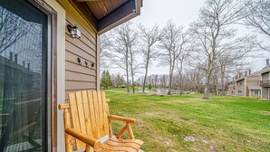 A wooden chair outside a building with a large window and a view of a grassy area with trees. - Cozy Ski Condo with Pond View (Hidden Valley)