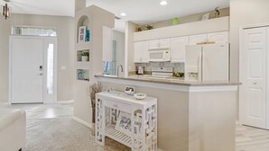 A modern kitchen with white cabinetry, a built-in microwave, and a refrigerator. There is a small island with a sink and a decorative vase. - Heron's Glen Beautiful Beachy Home in Gated Golf Community Home (North Fort Myers)