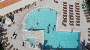 An aerial view of a swimming pool area with multiple pools, sun loungers, and a small deck area. - Heron's Glen Beautiful Beachy Home in Gated Golf Community Home (North Fort Myers)