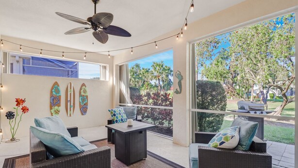 A sunlit patio with wicker furniture, string lights, and surfboards on the wall. - Heron's Glen Beautiful Beachy Home in Gated Golf Community Home (North Fort Myers)