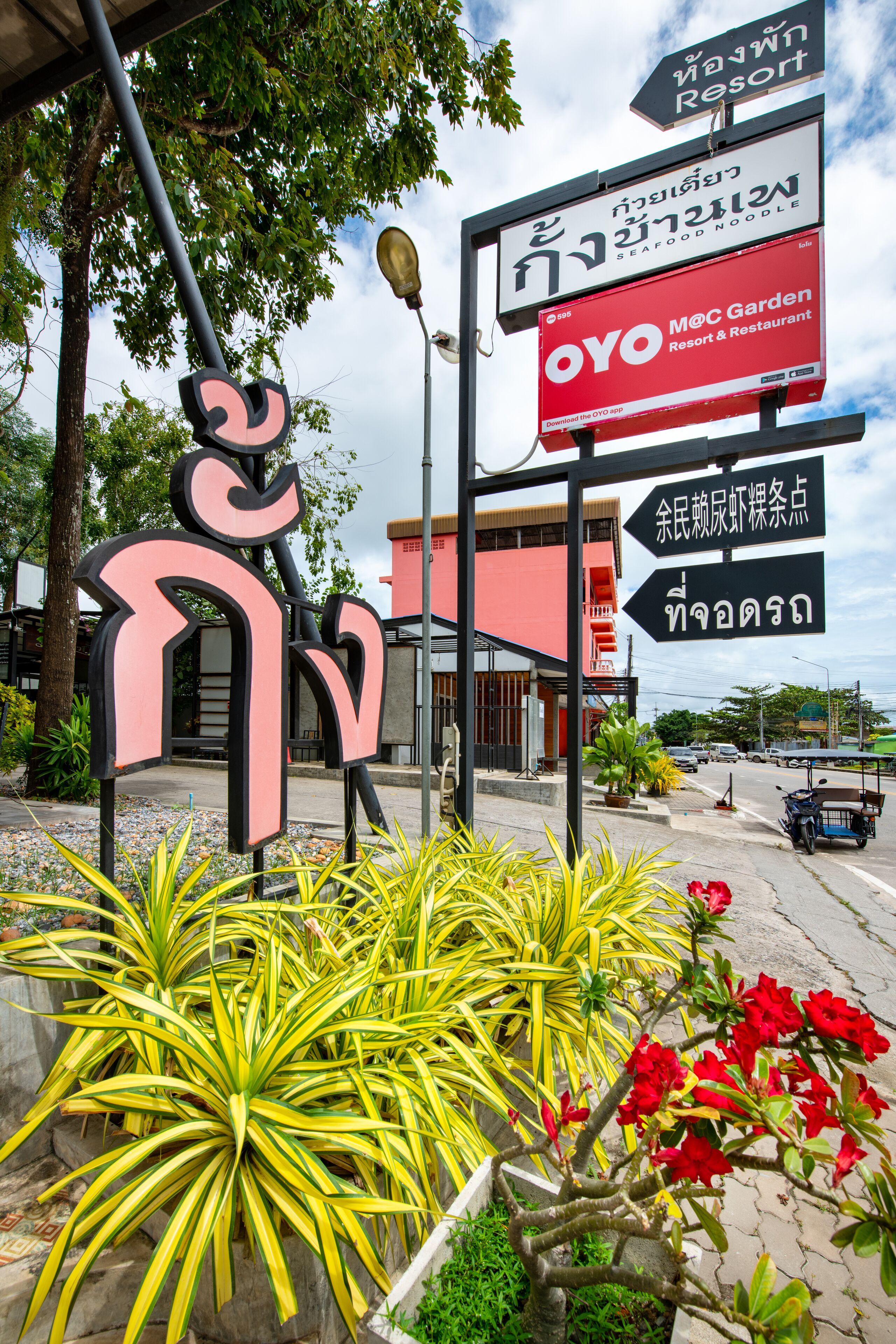 A sign for OYO M&C Garden Resort & Restaurant with directional arrows and Thai text.